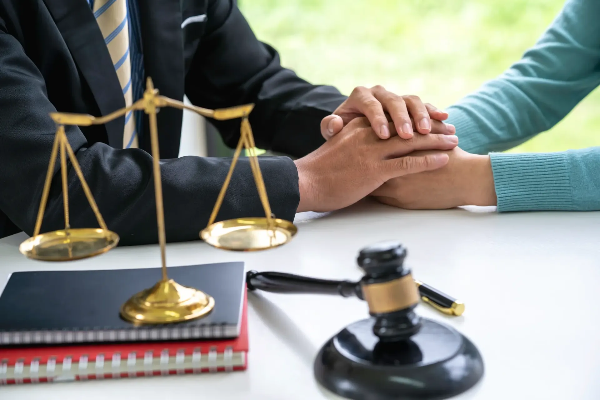 Weegschaal van Justitia op tafel met handen van een advocaat en cliënt